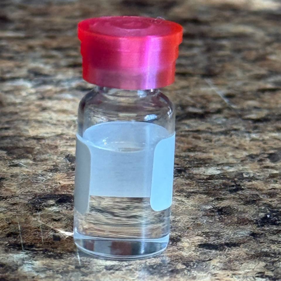 A pink-capped vial containing liquid through which the background is visible